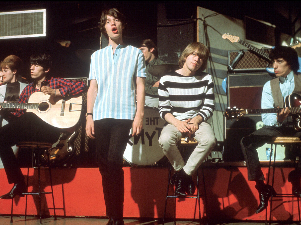 Это фото сделано в 1969 году, незадолго до смерти Брайана Джонса (в полосатой футболке) в возрасте 27 лет. Стоит Мик Джаггер, в клетчатой рубашке - Кит Ричардс, в жилете - Билл Уаймен